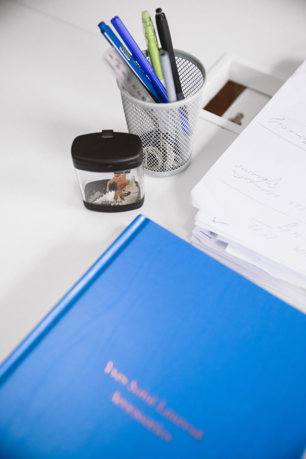 Clean desktop with a blue book, pen holder, and stationery, perfect for research and study.